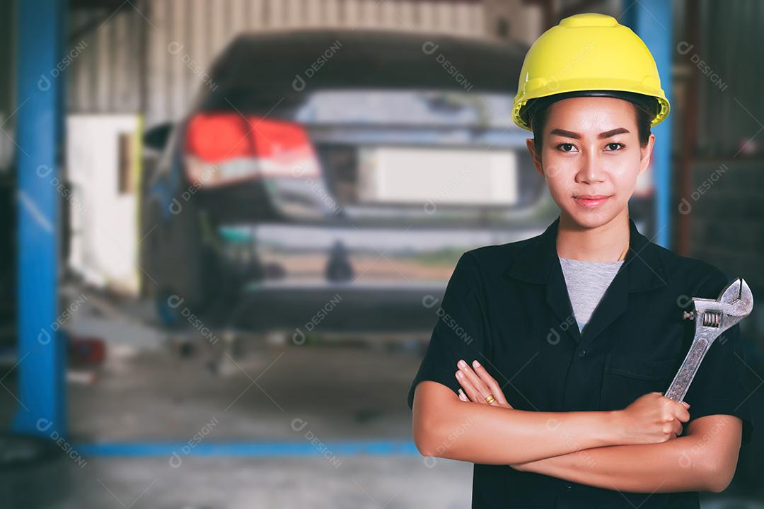 Retrato de uma jovem mecânica sorridente inspecionando um carro na oficina de automóveis