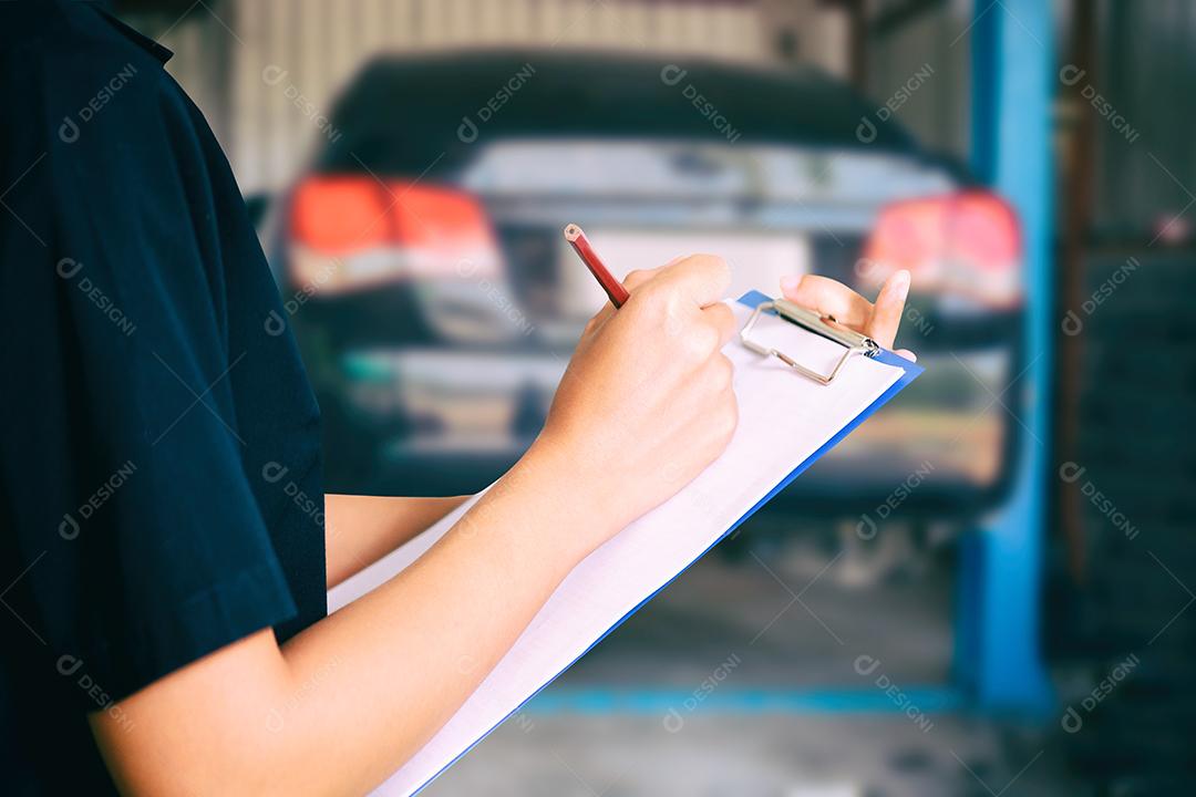 Retrato de uma jovem mecânica sorridente inspecionando um carro na oficina de automóveis
