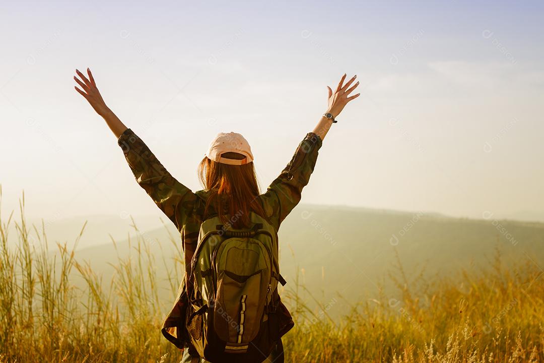 Mulher viajante da liberdade de pé com os braços levantados e desfrutando de uma bela natureza e torcendo o mochileiro jovem no pico da montanha à beira-mar do nascer do sol