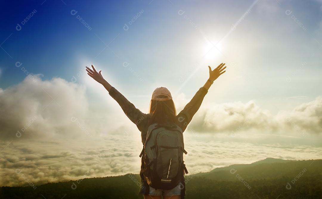 Mulher viajante da liberdade de pé com os braços levantados e desfrutando de uma bela natureza e torcendo o mochileiro jovem no pico da montanha à beira-mar do nascer do sol