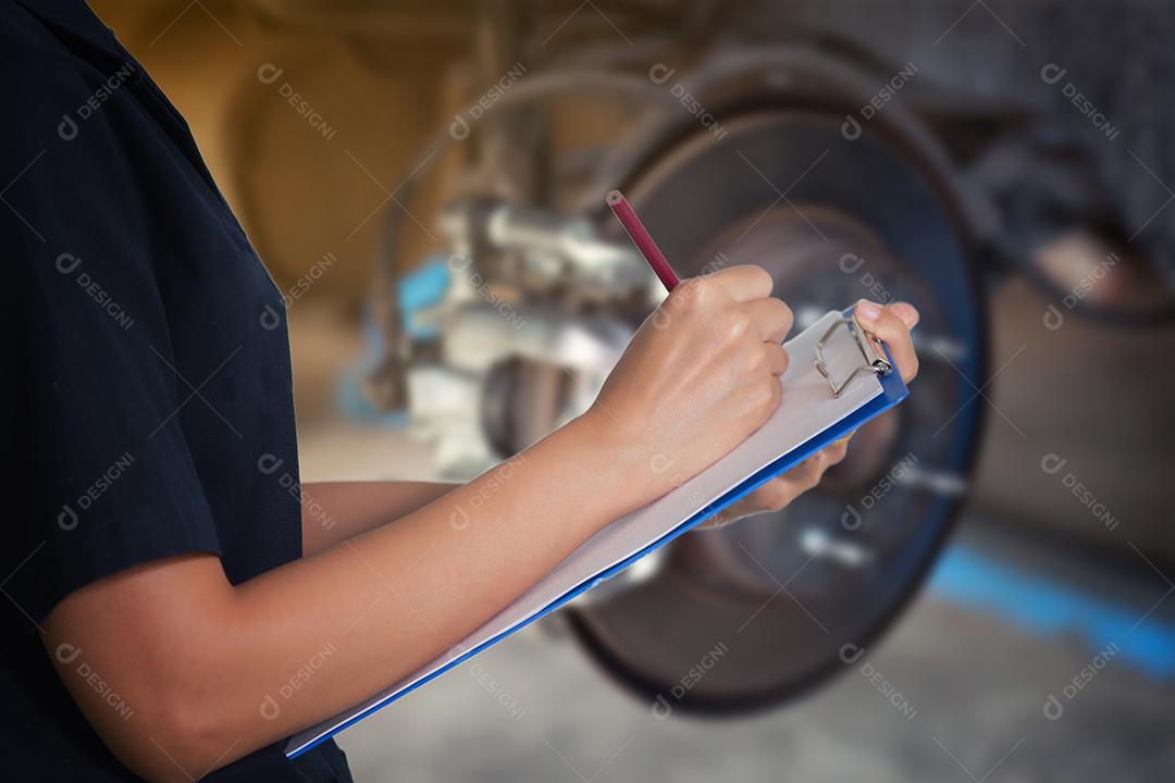 Engenheiras e técnicas asiáticas estão verificando mecânicos e inspecionando um disco de freio de roda de carro e sapatas de automóvel levantado na estação de serviço de reparo