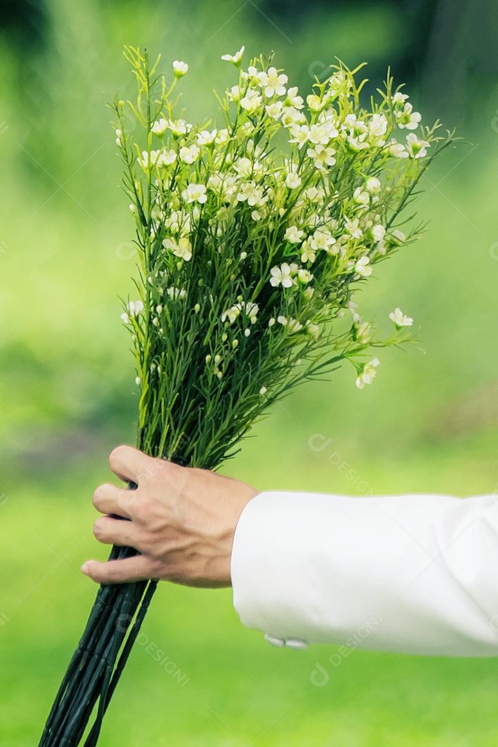 Mão do noivo está segurando um buquê de flores.