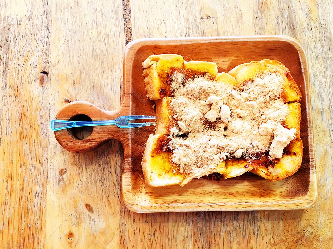 Pão torrado com carne de porco desfiada seca e pasta de pimentão em prato quadrado de madeira está na mesa de madeira