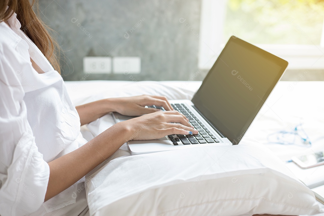 Mulher de negócios asiático usando notebook e sorrindo felizes por trabalhar na cama