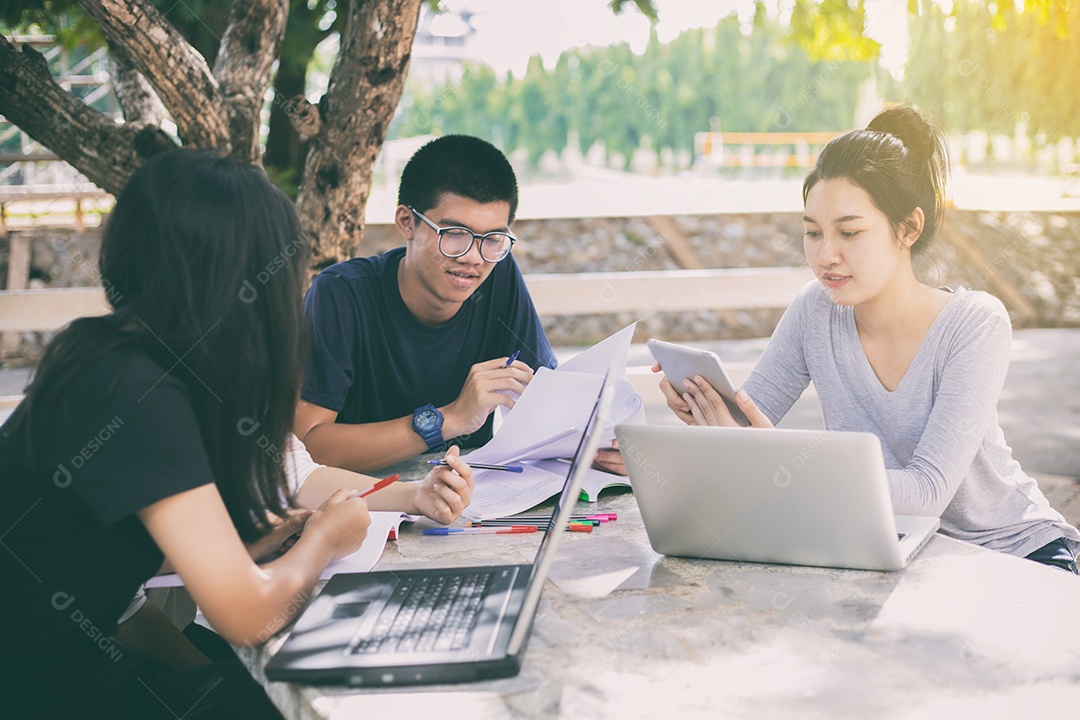 Grupo asiático de estudantes compartilhando ideias para trabalhar no gramado do campus