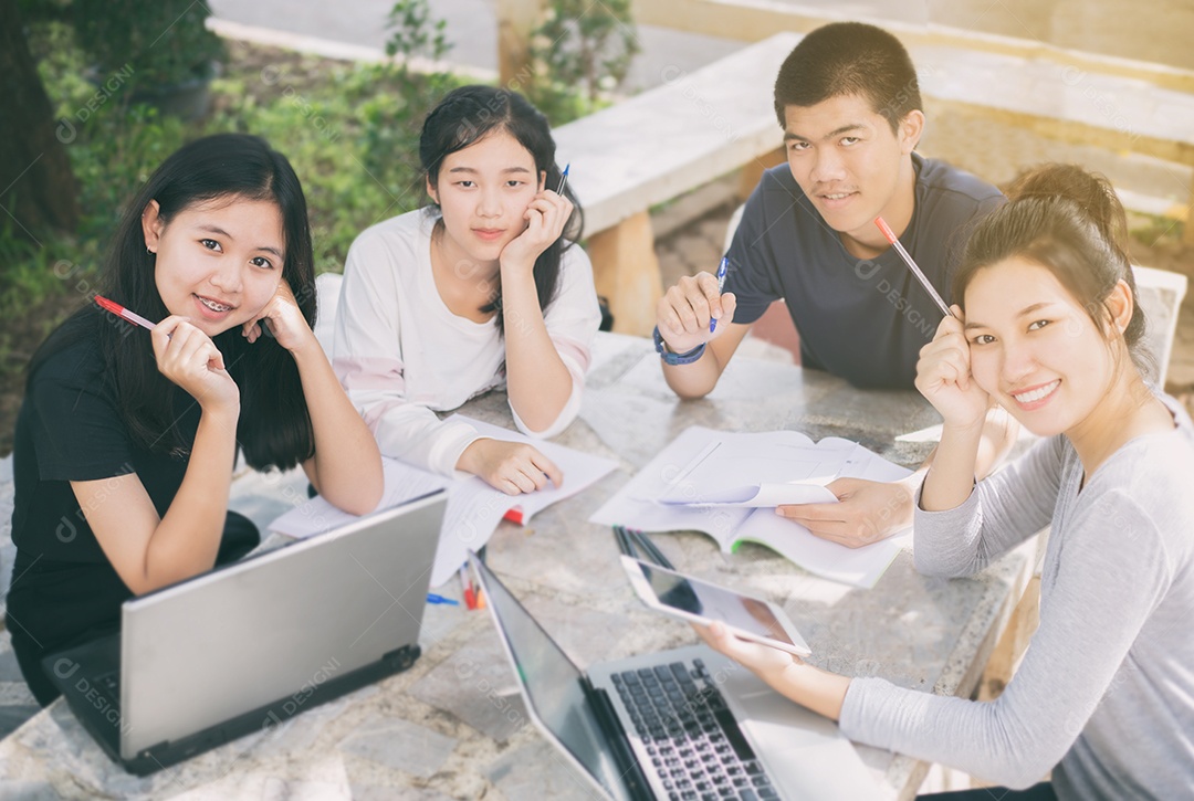 Grupo asiático de estudantes sorrindo e compartilhando ideias para trabalhar no gramado do campus