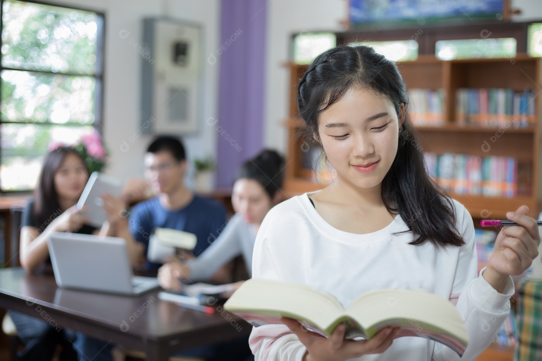 Estudantes asiáticas segurando para seleção Livro na biblioteca