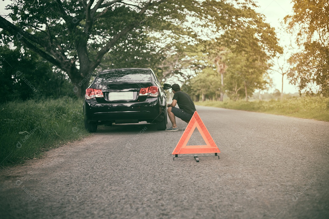 Homem estressado sentado após uma avaria de carro com triângulo vermelho de um carro na estrada