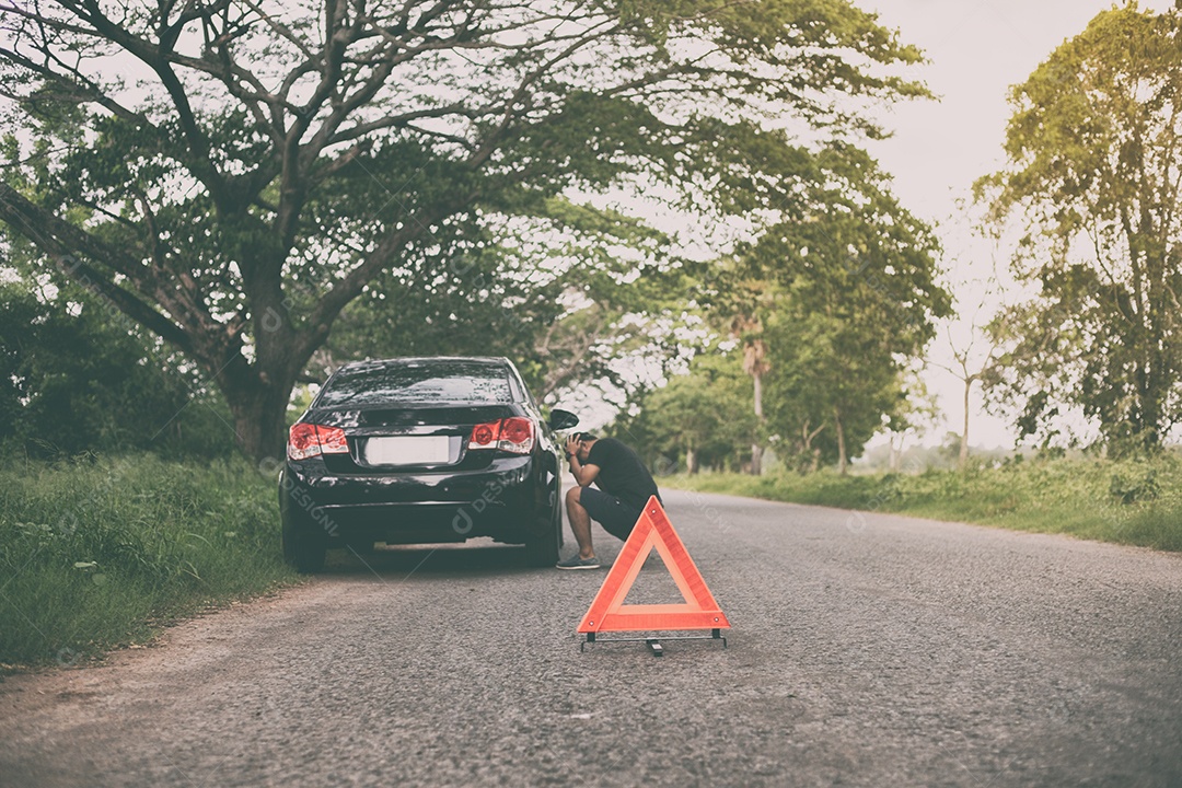 Homem estressado sentado após uma avaria de carro com triângulo vermelho de um carro na estrada