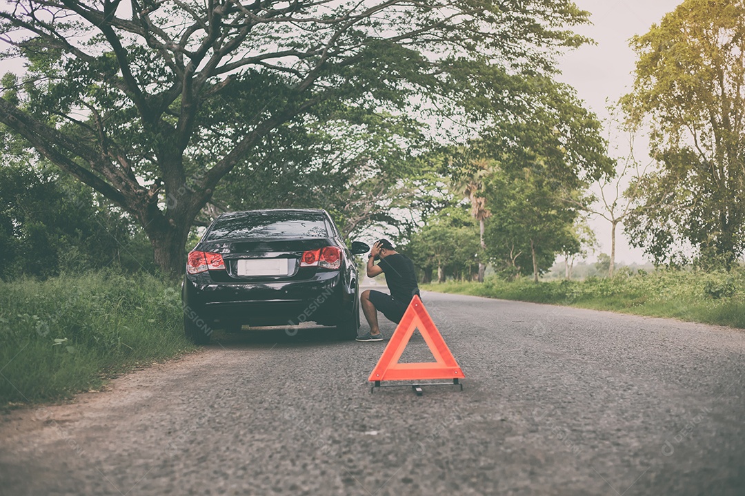 Homem estressado sentado após uma avaria de carro com triângulo vermelho de um carro na estrada