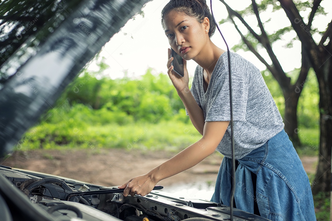 Mulher asiática usando telefone celular enquanto olha para o carro quebrado na rua