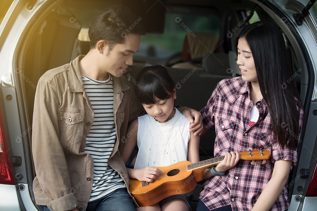 menina feliz tocando ukulele com família asiática sentado no carro para desfrutar de viagem e férias de verão