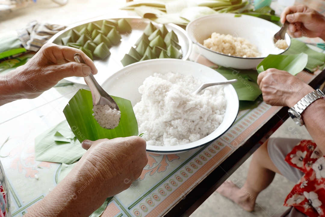 Homem e mulher são confederados para embrulhados em doces locais com folha de bananeira por ocasião do Dia da Família e do Festival Songkran da Tailândia
