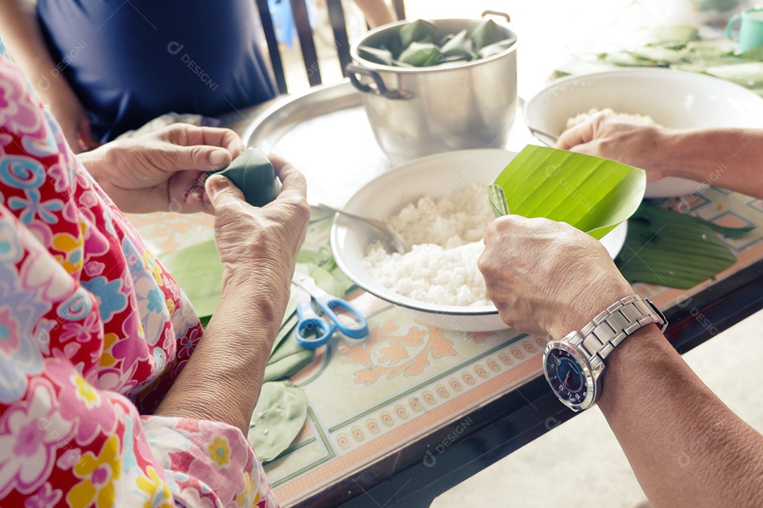 Homem e mulher são confederados para embrulhados em doces locais com folha de bananeira por ocasião do Dia da Família e do Festival Songkran da Tailândia