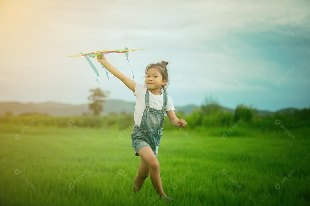 Menina asiática com uma pipa correndo e feliz no prado no verão na natureza