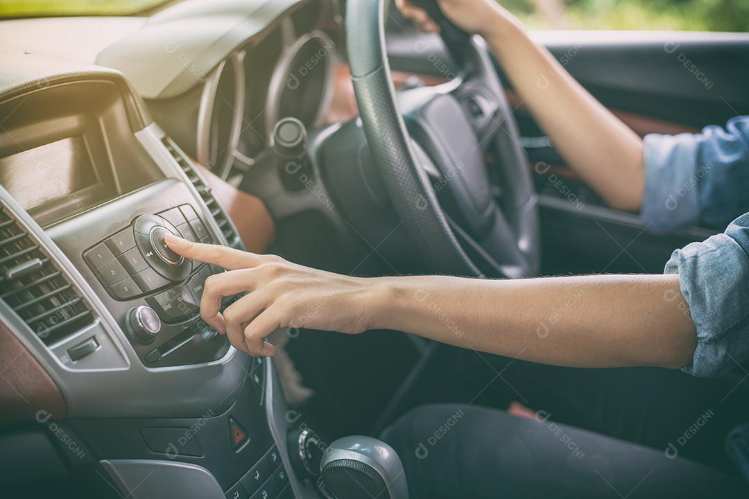 Mulher asiática pressionam o botão no rádio do carro para ouvir música.