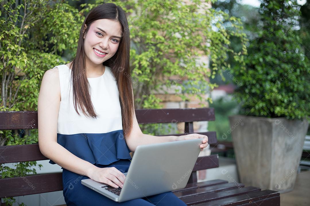 Mulher de negócios asiáticos usando notebook e sorrindo felizes por trabalhar ao ar livre