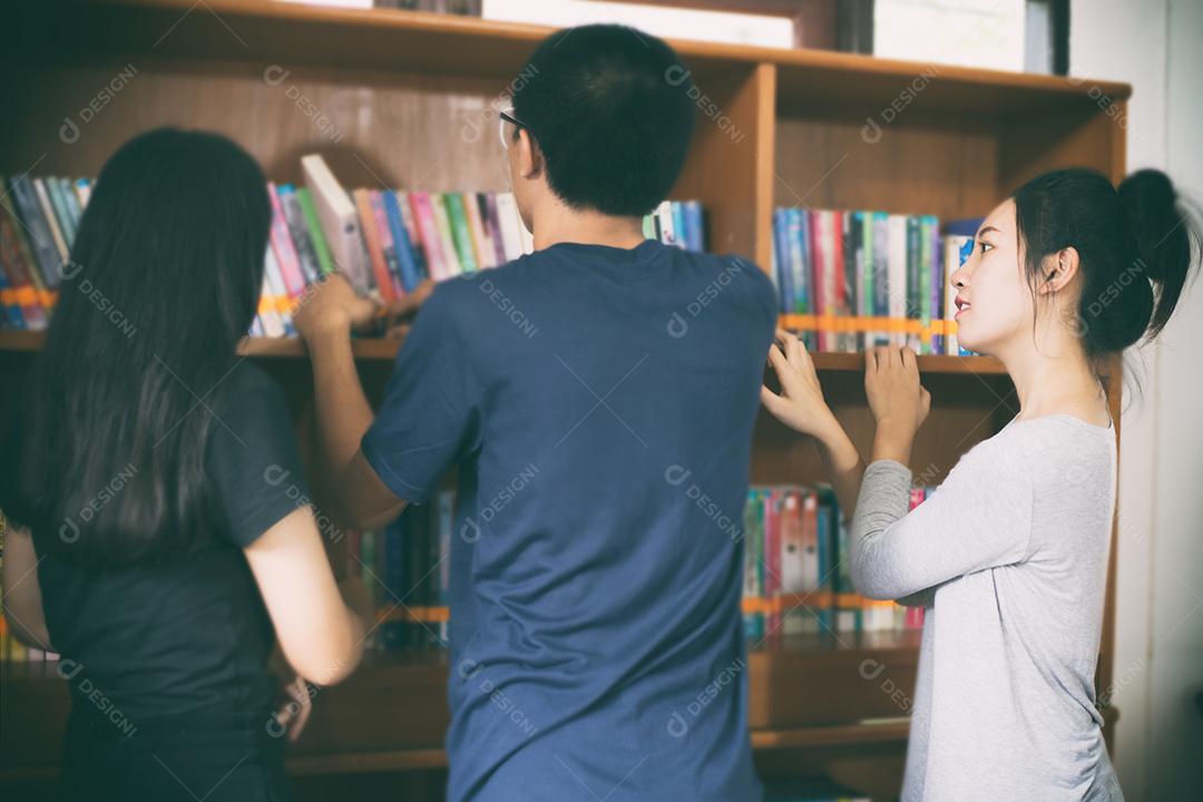 Estudantes asiáticas segurando para seleção Livro na biblioteca