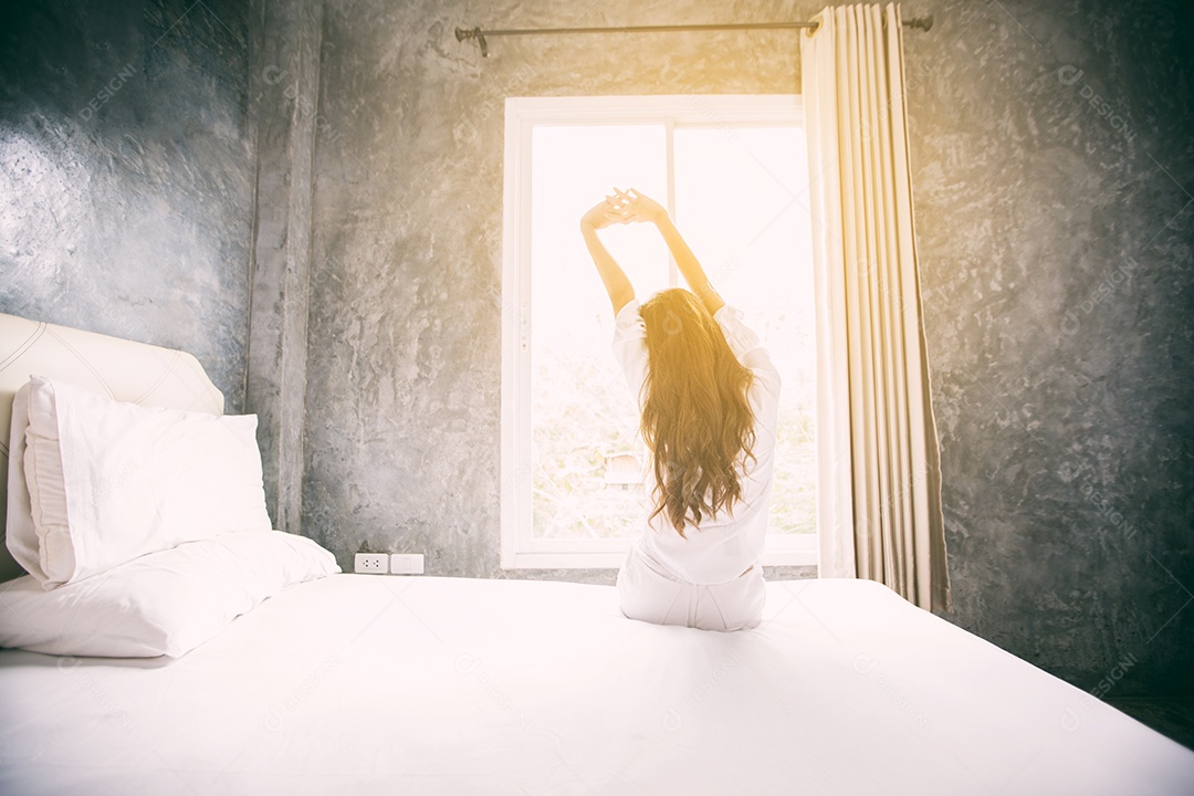 Mulher asiática acordando em sua cama totalmente descansada e abre as cortinas de manhã para tomar ar fresco.