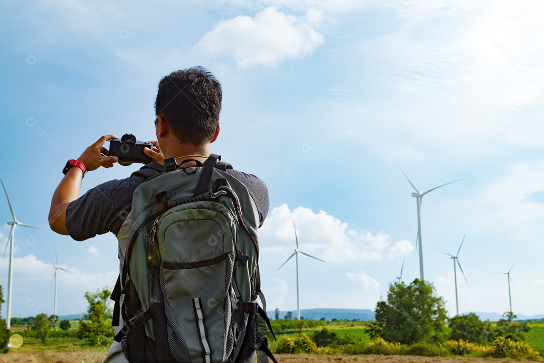 Homem asiático com mochila tirando uma foto em vista da turbina eólica.