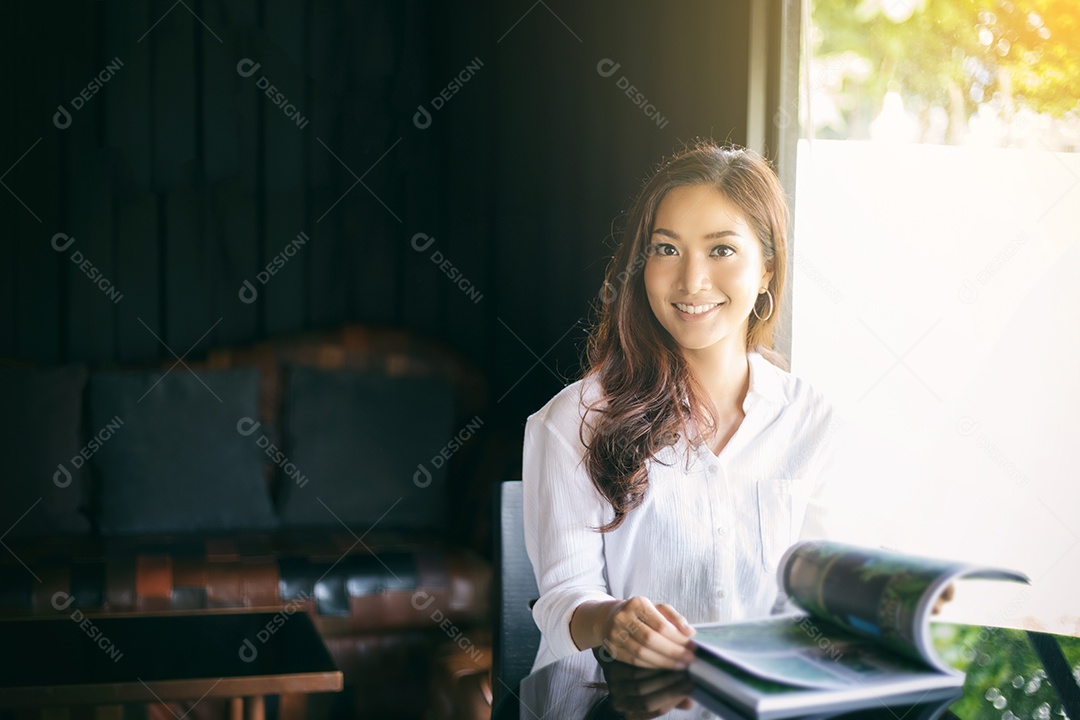 Mulher asiática sorrindo e lendo um livro para relaxar no café