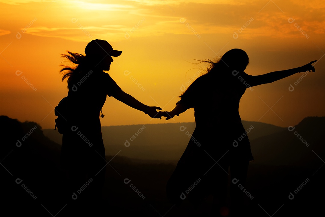 Casal de silhueta segurando a mão para viajantes no nascer do sol