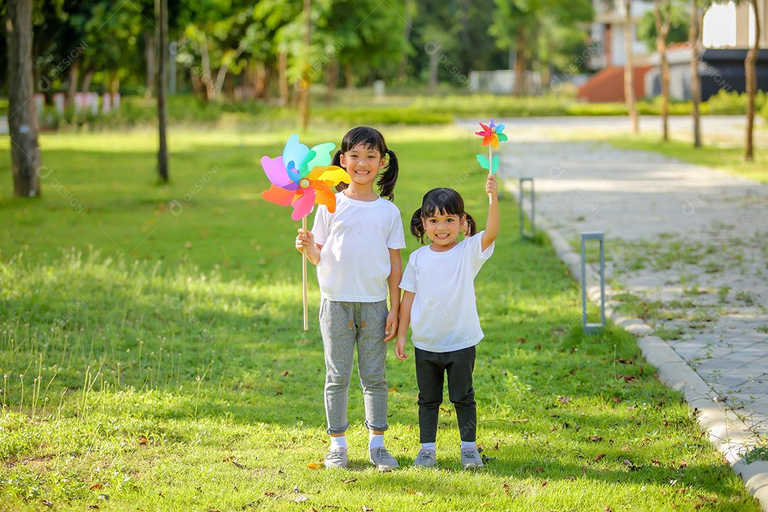 Duas meninas bonitinhas asiáticas brincando no moinho de brinquedo colorido