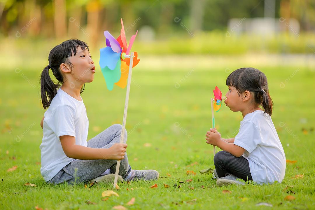 Duas meninas bonitinhas asiáticas brincando no moinho de brinquedo colorido