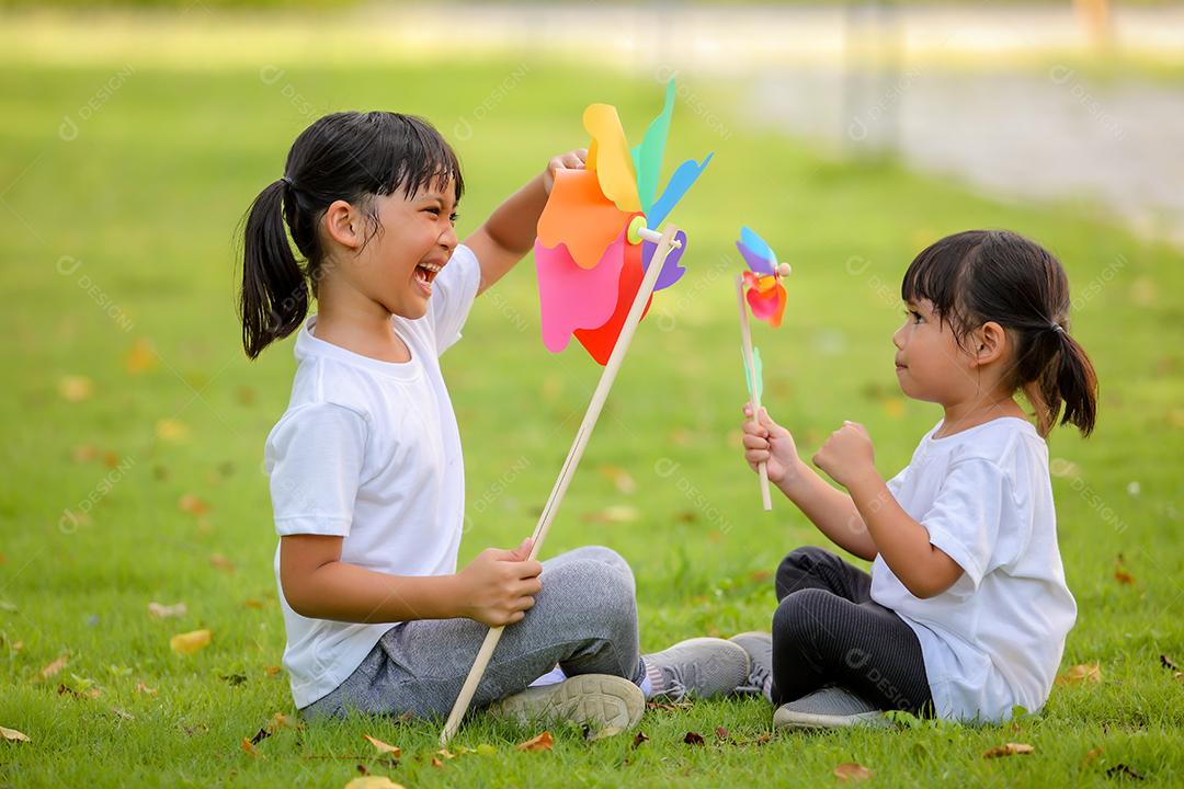 Duas meninas bonitinhas asiáticas brincando no moinho de brinquedo colorido