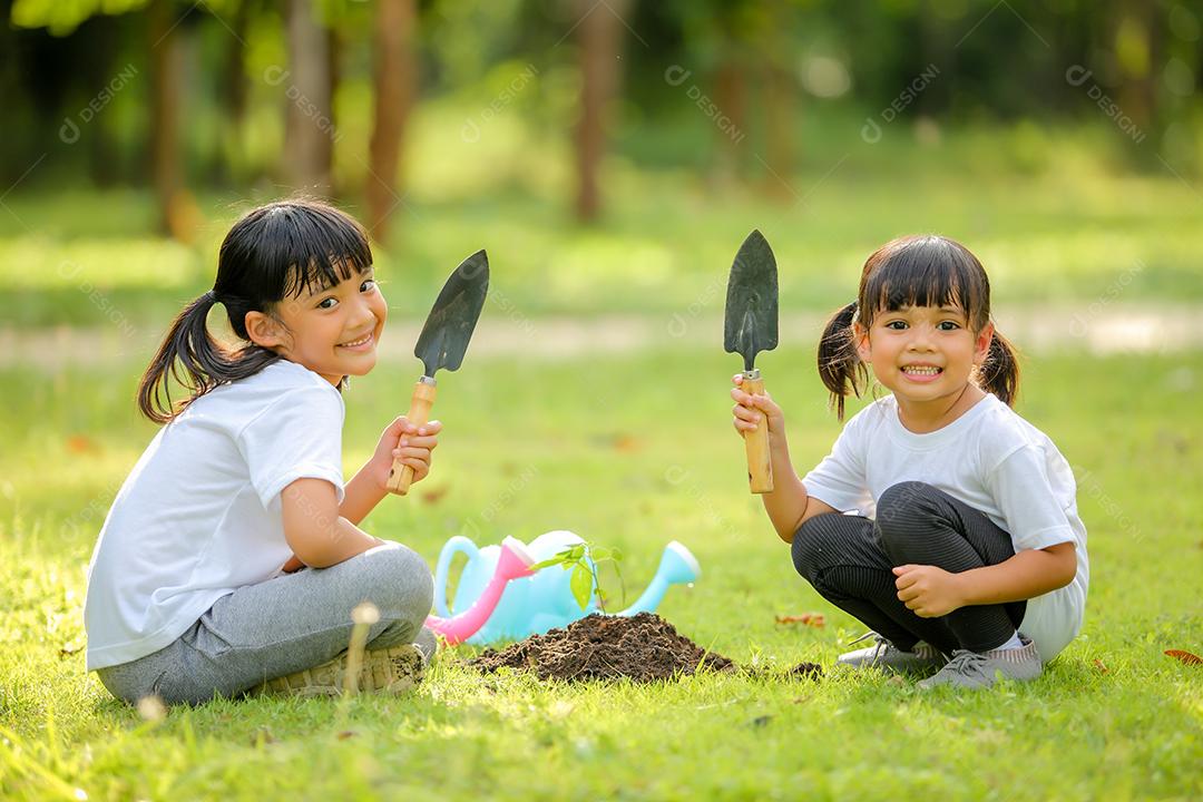 Meninas bonitinhas Asiáticas plantando árvore em solo preto no parque.