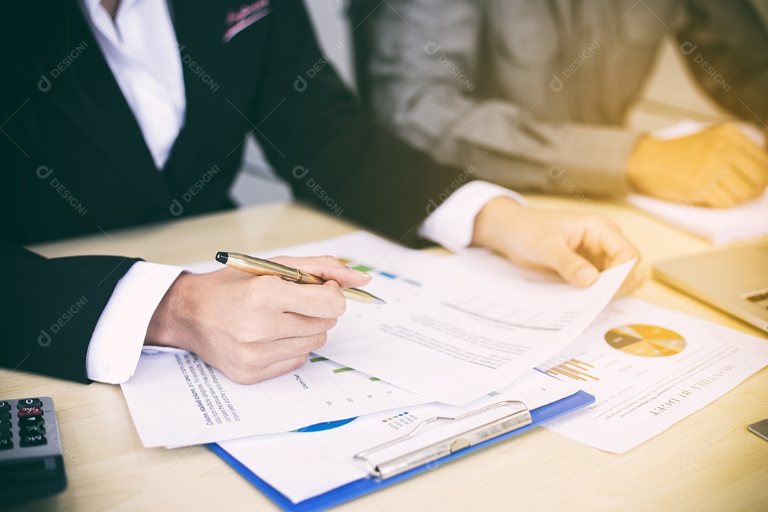 Empresárias asiáticas segurando uma caneta e documentos de análise na mesa de escritório com computador portátil e diagrama financeiro gráfico trabalhando em segundo plano