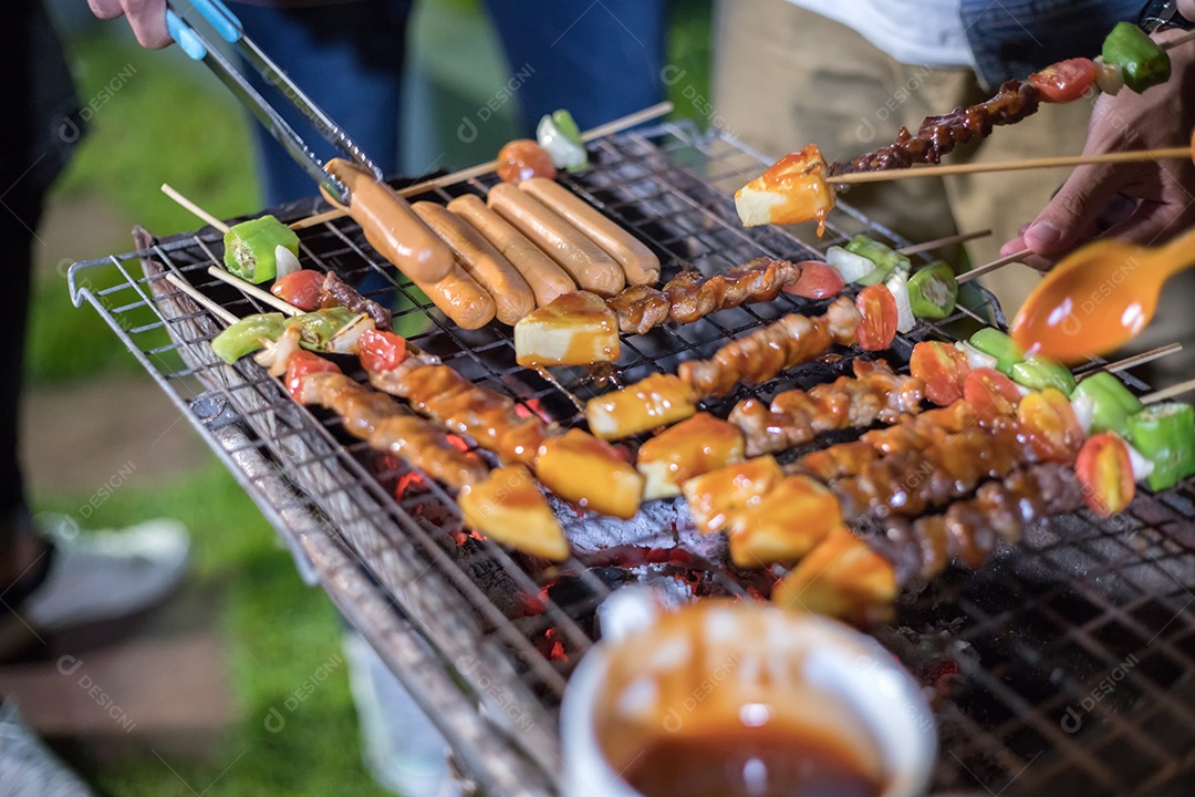 Grupo asiático de amigos fazendo churrasco e shashliks grelhados na festa grelhada no jardim ao ar livre