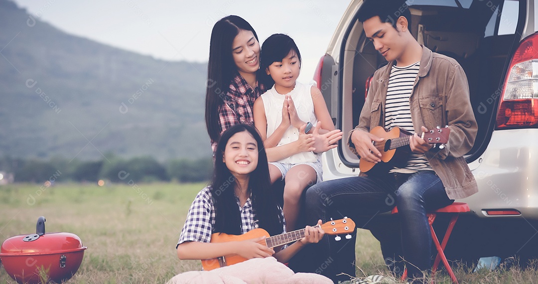 menina feliz tocando ukulele com família asiática sentada no carro para desfrutar de viagem e férias de verão