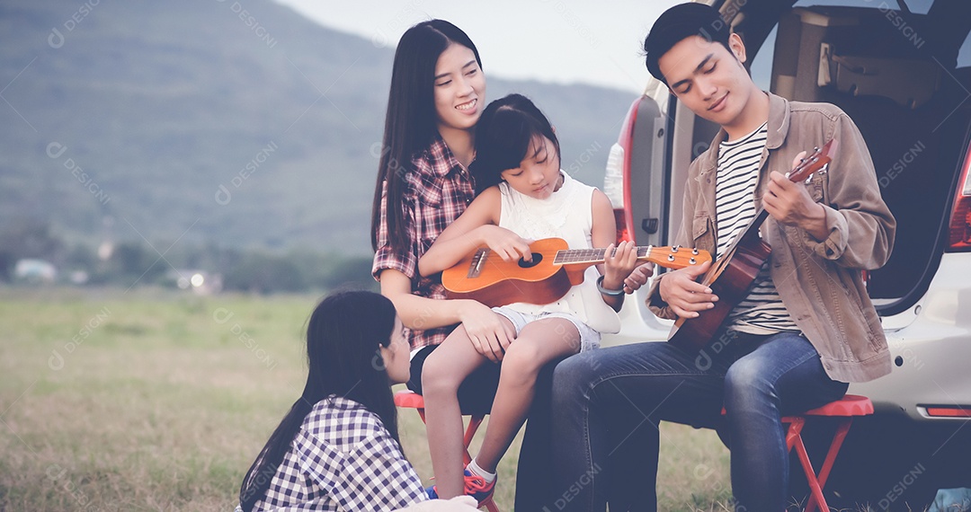 menina feliz tocando ukulele com família asiática sentada no carro para desfrutar de viagem e férias de verão