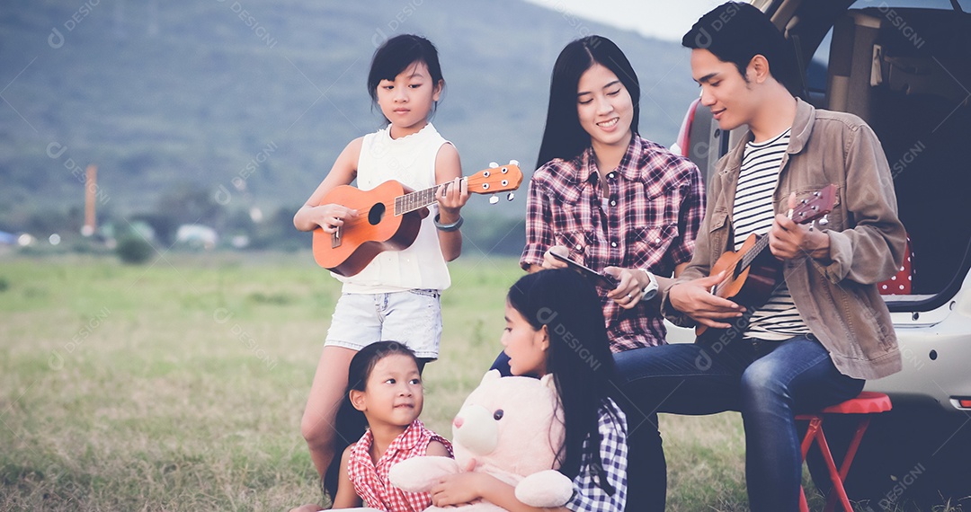 menina feliz tocando ukulele com família asiática sentada no carro para desfrutar de viagem e férias de verão