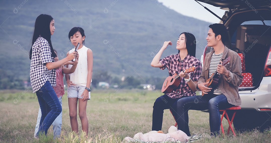 menina feliz tocando ukulele com família asiática sentada no carro para desfrutar de viagem e férias de verão