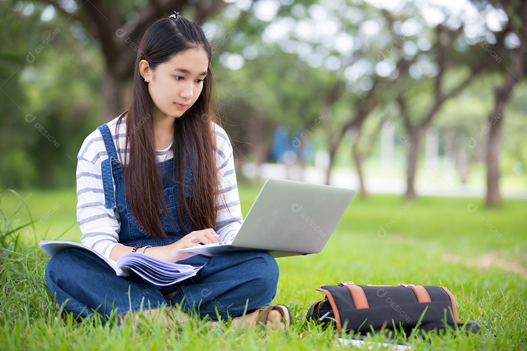 Linda garota asiática sorridente lendo livro e trabalhando na árvore no parque no verão para relaxar