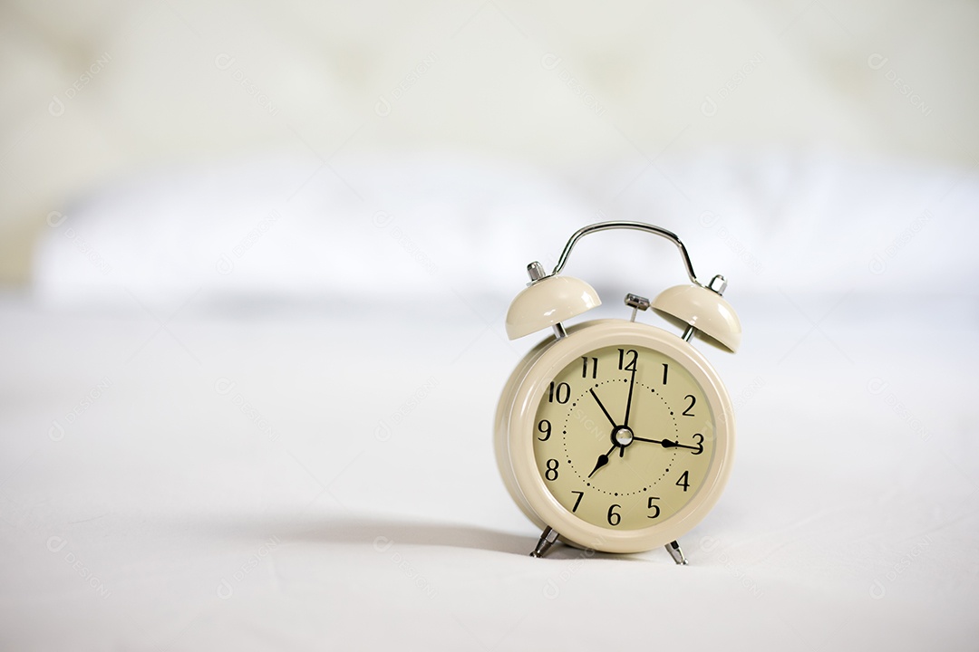 Despertador analógico na cama branca, hora da manhã com um sol brilhante