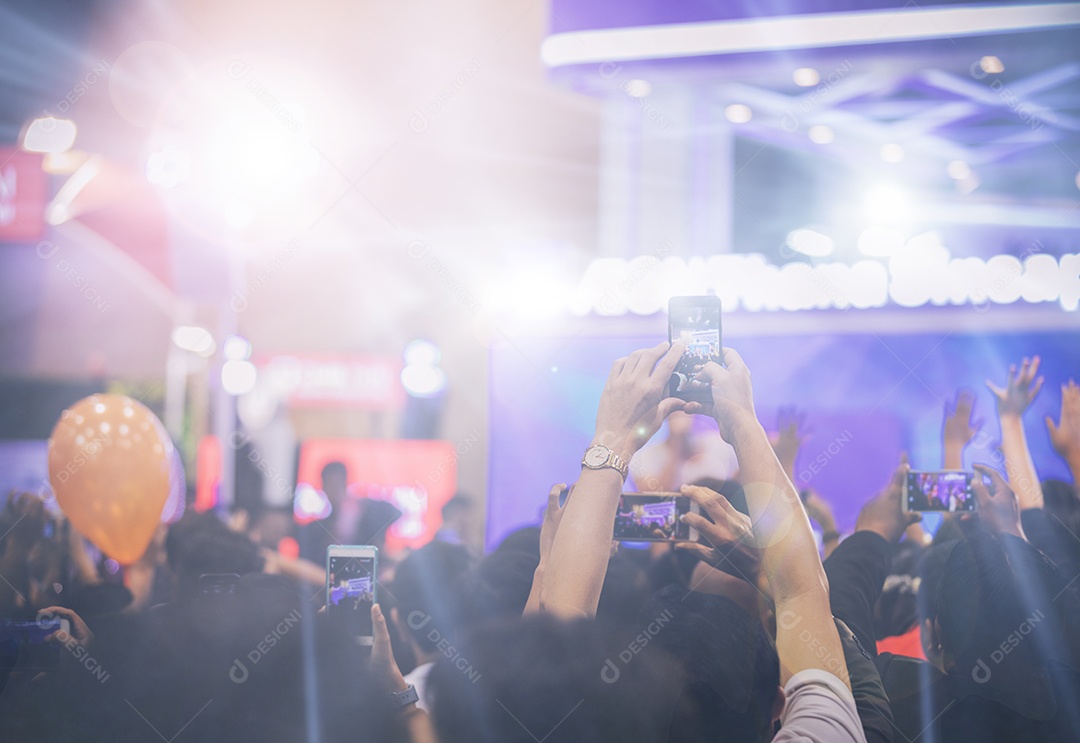 Mulher asiática segurando telefone inteligente e tela de toque para tirar fotos na multidão nas luzes do palco do concerto, fundo embaçado