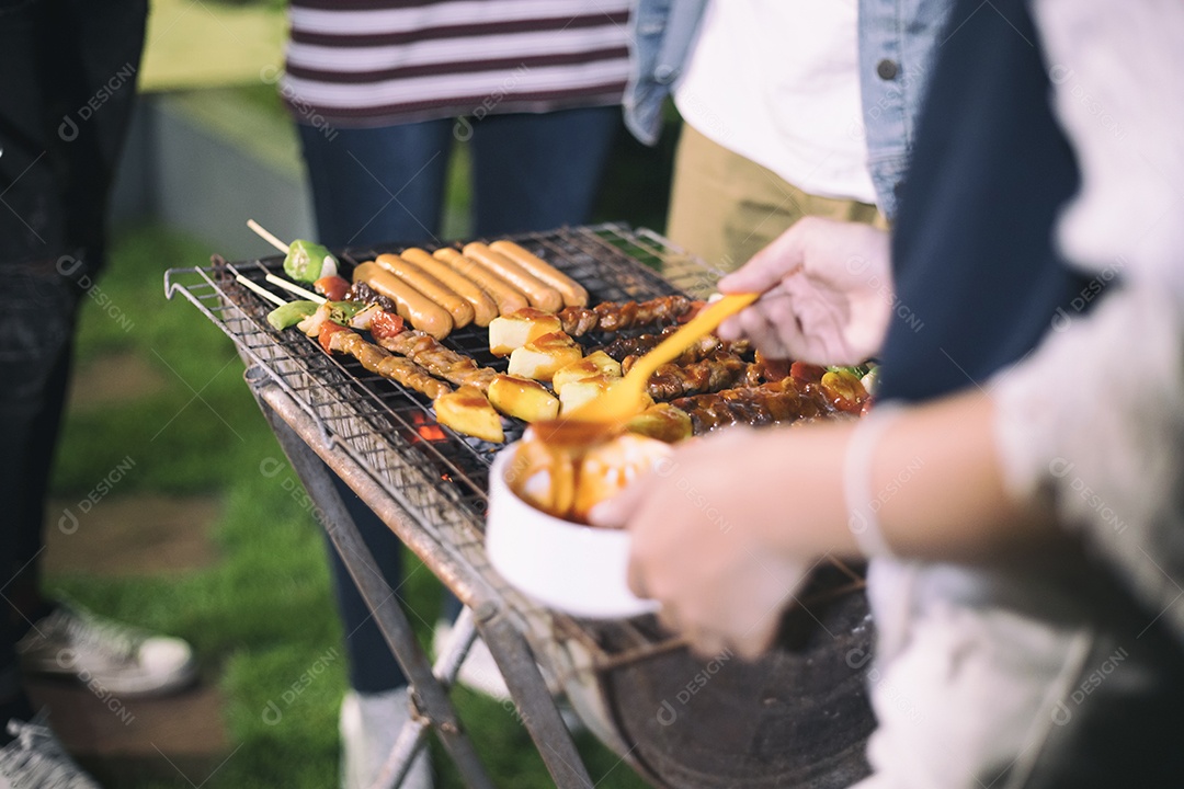 Grupo asiático de amigos fazendo churrasco e shashliks grelhados na festa grelhada no jardim ao ar livre