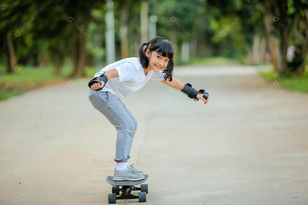 Menina bonitinha asiática andando de skate no parque de skate.