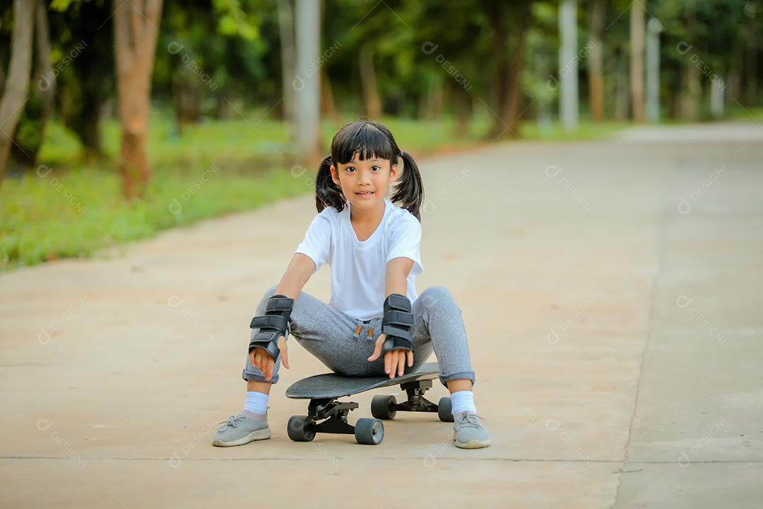 Menina bonitinha asiática andando de skate no parque de skate.