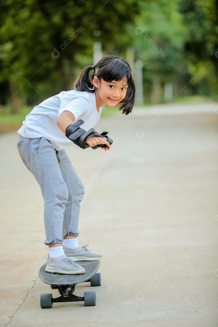 Menina bonitinha asiática andando de skate no parque de skate.