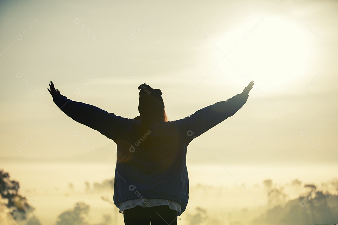 Silhueta de mulher viajante da liberdade de pé com os braços levantados e desfrutando de uma bela natureza e torcendo jovens ao pôr do sol e nevoeiro