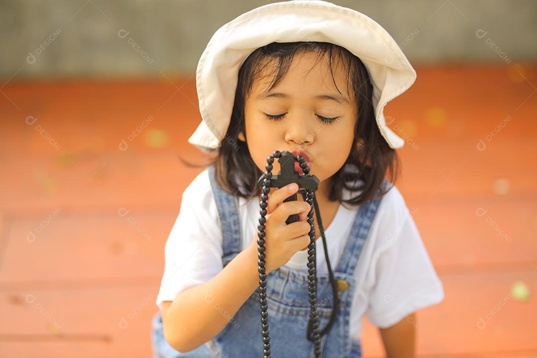 Menina asiática rezando a bênção de Deus e segurando a cruz de madeira