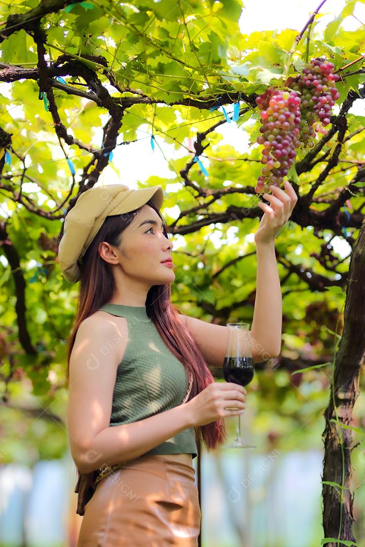 Mulher asiática segurando um cacho de uva em um vinhedo.