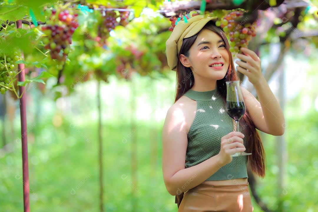 Mulher asiática com copo de vinho tinto no vinhedo em suas férias.