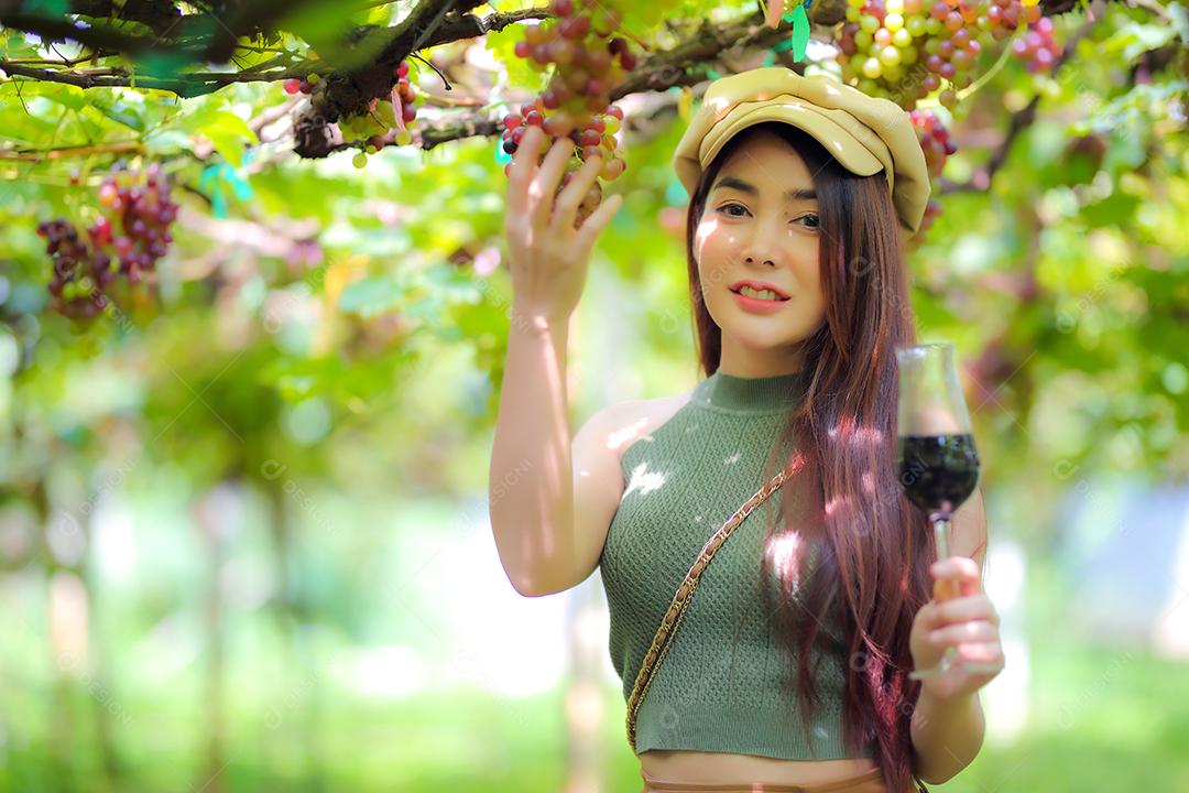 Mulher asiática com copo de vinho tinto no vinhedo em suas férias.