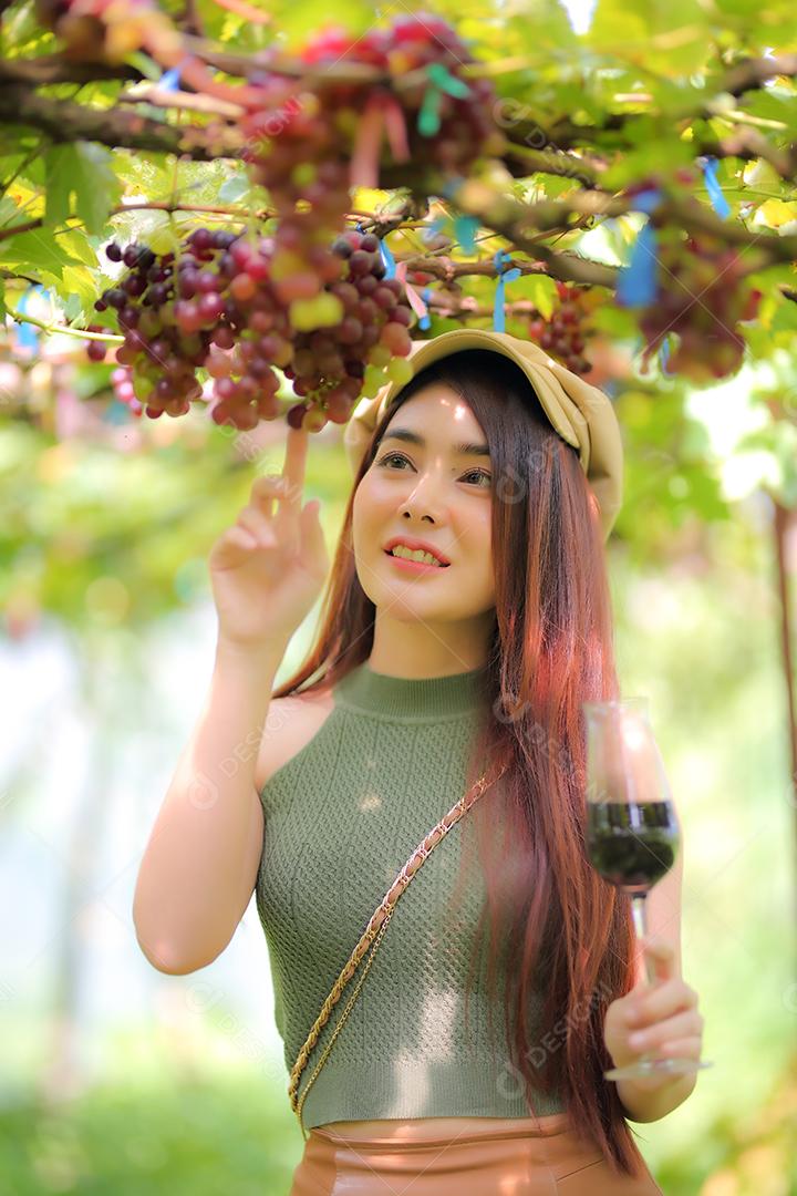 Mulher asiática com copo de vinho tinto no vinhedo em suas férias.
