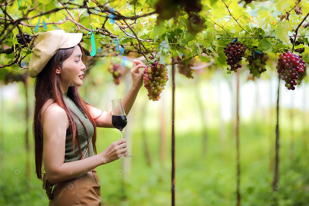 Mulher asiática com copo de vinho tinto no vinhedo em suas férias.